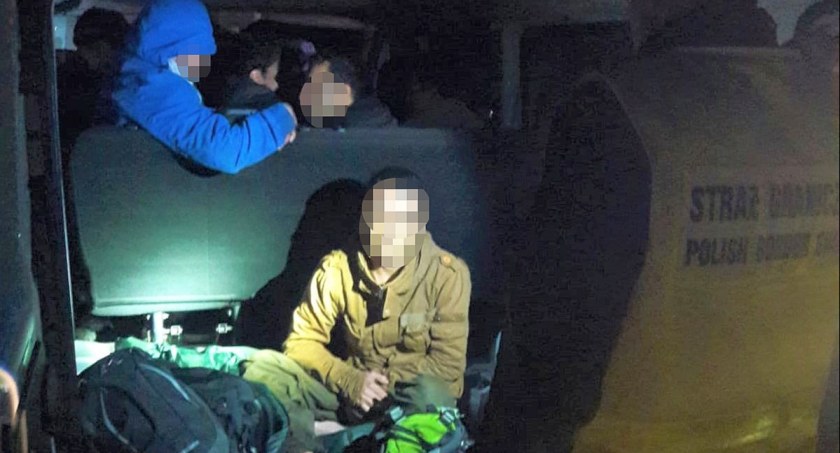 Nocne zdjęcie osób z zamaskowanymi twarzami, z torbami i plecakami, na siedzeniach i podłodze busa