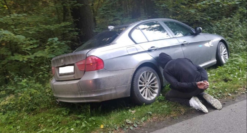 Zdjęcie zatrzymanego, klęczącego ze skutymi rękami przy aucie
