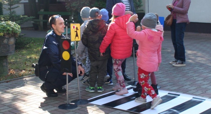 Zdjęcie policjanta z dziećmi przechodzącymi przez makietę przejścia dla pieszych