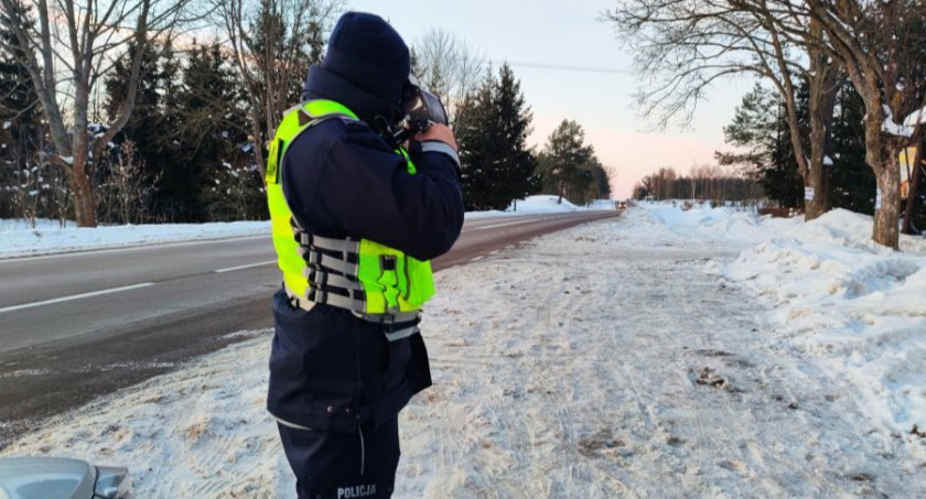 Zdjęcie policjanta przy trasie zimą, dokonującego pomiaru radarem