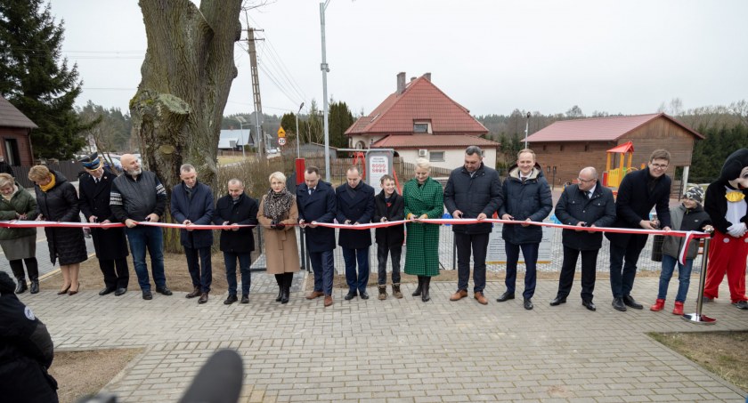 Zdjęcie dorosłych i dzieci na wyłożonym kostką placu z zabawkami plenerowymi