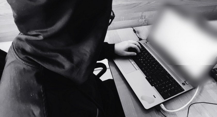 Zdjęcie zakapturzonej postaci przed laptopem z zamaskowanym ekranem