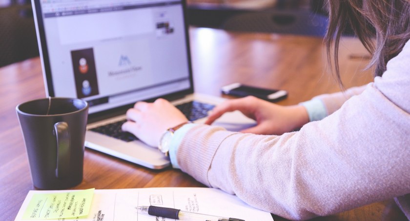 Zdjęcie kobiety siedzącej przy laptopie z dokumentami i kubkiem napoju