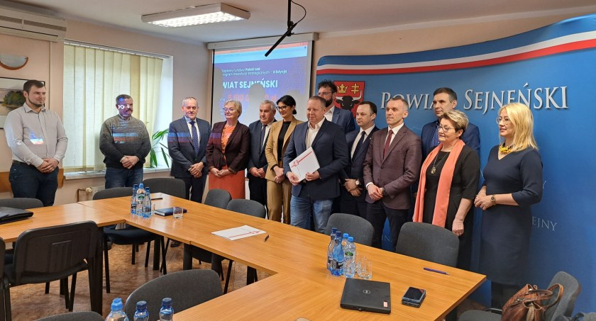 Zdjęcie grupy osób stojących na tle ścianki w sali konferencyjnej