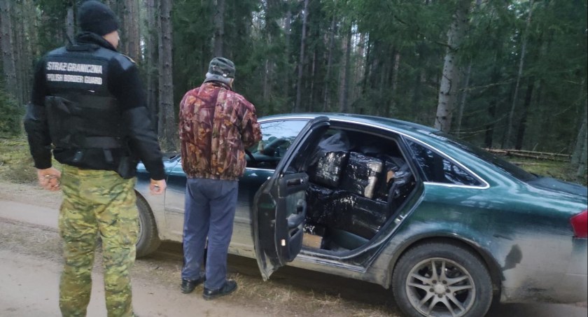 Zdjęcie pogranicznika i mężczyzny, stojących tyłem przy aucie z otwartymi drzwiami