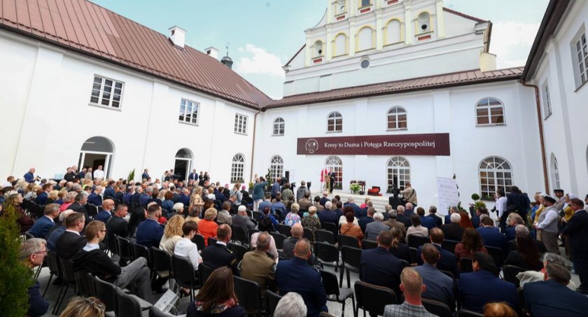 Zdjęcie osób siedzących przed sceną w wirydarzu klasztoru w Sejnach, na scenie minister kultury