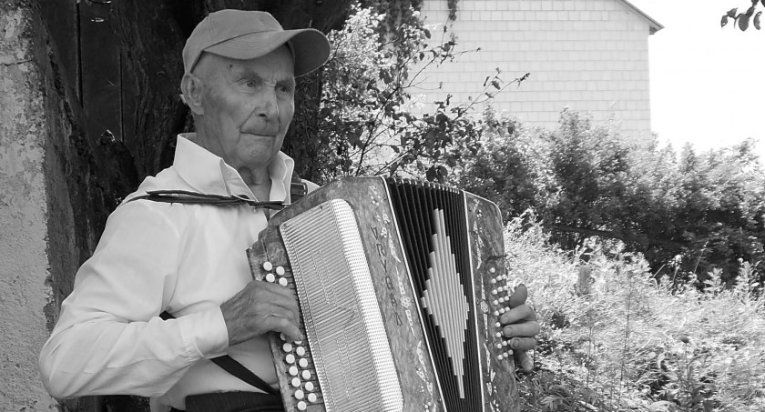 Zdjęcie starszego mężczyzny siedzącego na stołku, grającego na harmonii guzikówce